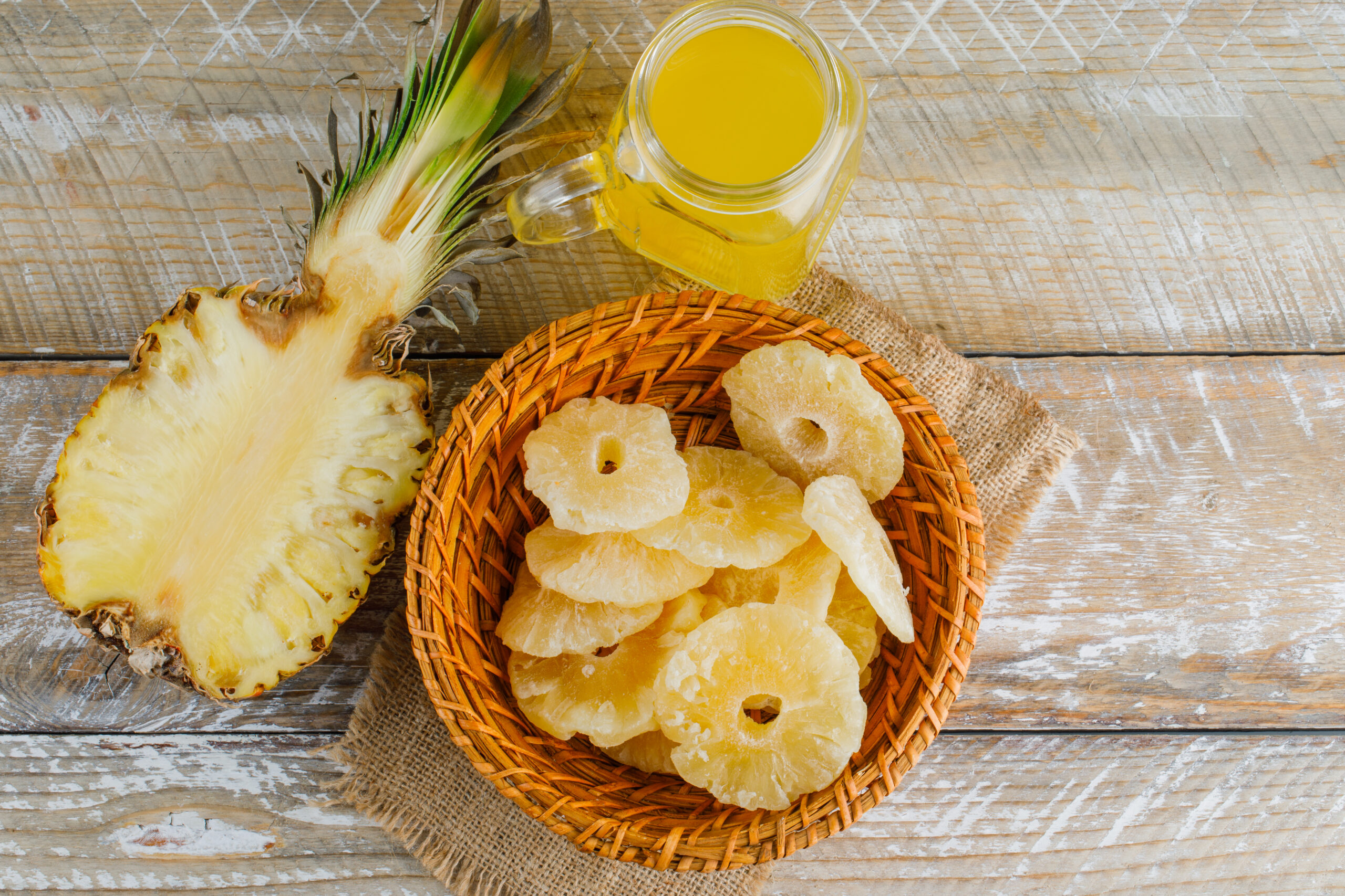 Pineapple with juice, candied rings on wooden and piece of sack background, flat lay.